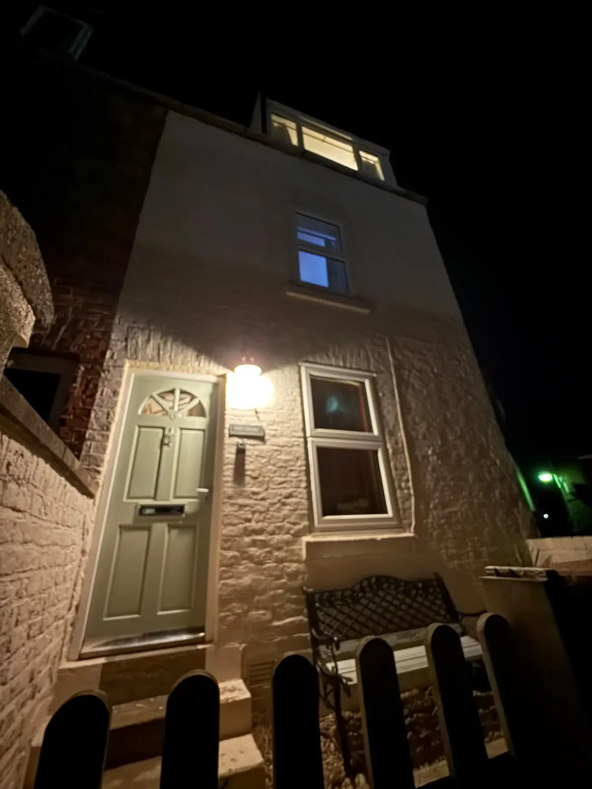 Night-time front of Pipit House with a sage-green door and porch light